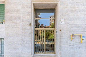 A building entrance with a metal gate, a window with a view of the street, and a sign on the wall.