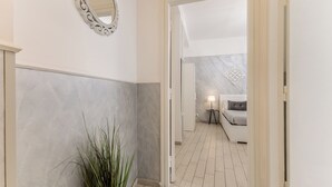 A hallway with a mirror, a plant, and a view into a bedroom with a bed and a lamp. - Few steps from Vatican City - 2 double rooms (Roma)