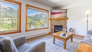 A living room with a stone fireplace, large windows with mountain views, and a cozy seating area. - Heart of Canmore - Pet Friendly with Shared Rooftop Hot Tub (Canmore)