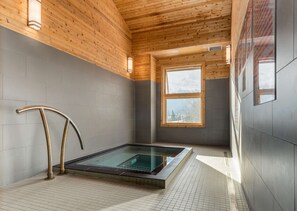 Een moderne spa ruimte met een glazen hottub, houten plafond en grote ramen.