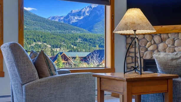 A room with a view of mountains, a stone fireplace, and a table with a lamp. - Heart of Canmore - Pet Friendly with Shared Rooftop Hot Tub (Canmore)