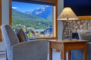 Una habitación con vista a las montañas, chimenea de piedra y una mesa con lámpara.