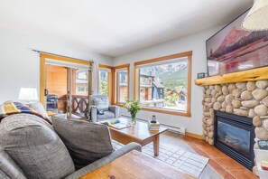 A cozy living room with a fireplace, large windows, and a view of a mountain landscape.