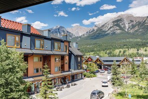 A mountain town with a hotel featuring balconies, a parking area, and a view of the mountains.
