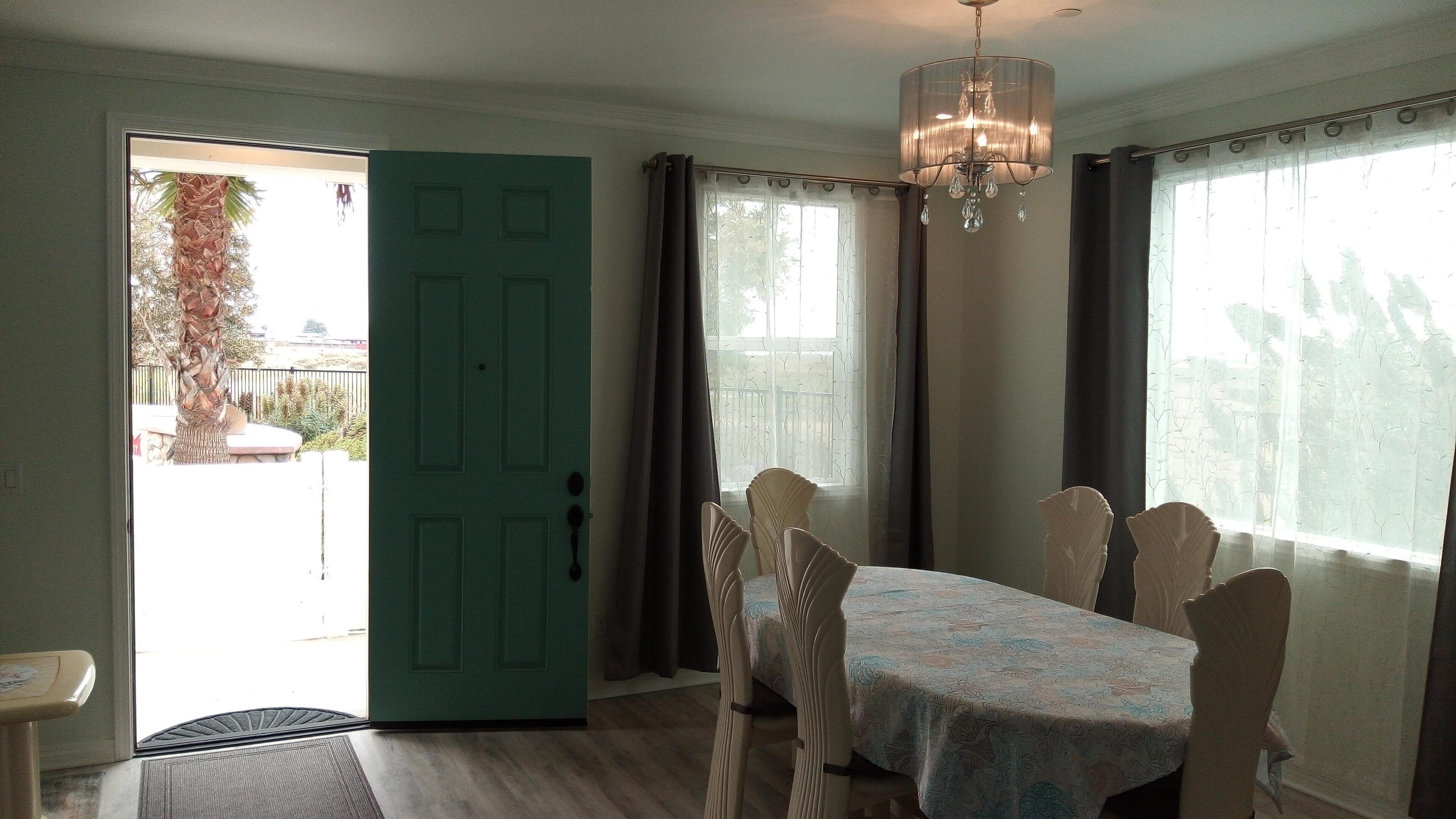 A dining area with a table set for six, a chandelier, and a door leading outside.
