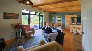 A spacious living area with a wooden ceiling, a black leather sofa, a wooden coffee table, and a dining area with a table and chairs. - Hahei Hideout Retreat - private and surrounded by bush. Pond and small orchard (Hahei)
