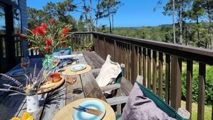 A wooden deck with a table set for dining, surrounded by a wooden railing, overlooking a forested landscape. - Hahei Hideout Retreat - private and surrounded by bush. Pond and small orchard (Hahei)