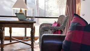 A cozy living room with a leather sofa, a wicker chair, a wooden table with a laptop, and a window with curtains. - Meadow House 7 / 2 BR / 2 BA Sleeps 6+ (Sunriver)