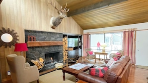 A cozy living room with a stone fireplace, a mounted deer head, a leather sofa, and a wooden coffee table. - Meadow House 7 / 2 BR / 2 BA Sleeps 6+ (Sunriver)
