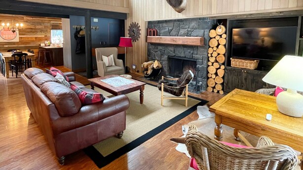 A spacious living room with a fireplace, leather sofa, and a mounted deer head. - Meadow House 7 / 2 BR / 2 BA Sleeps 6+ (Sunriver)