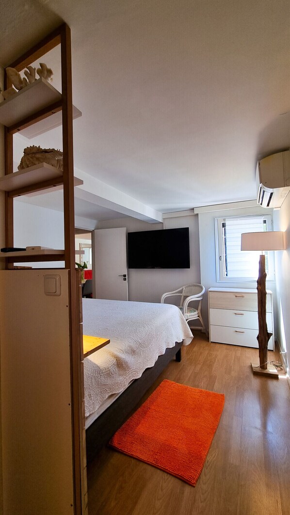 A compact bedroom with a bed, a desk, a chair, a TV, and a window.