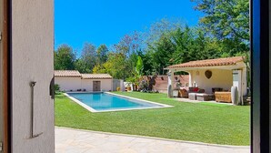 A view through a glass door into a backyard with a swimming pool, stone patio, and outdoor furniture.