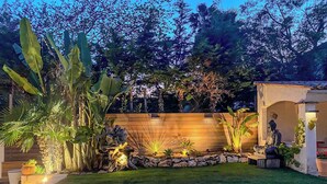 A well-maintained garden with a wooden fence, a Buddha statue, and various plants.