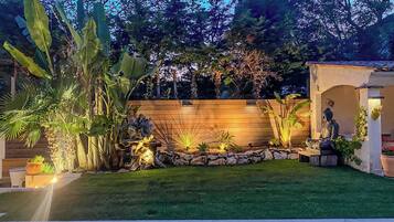 A well-maintained garden with a wooden fence, a Buddha statue, and various plants.