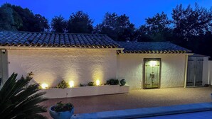 A house with a tiled roof, a door with a light, and a small garden area with plants.