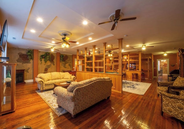 A spacious living room with wooden flooring, a fireplace, and a large bookshelf.