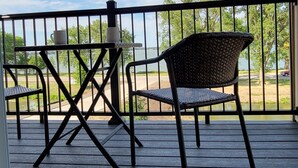 Un espace extérieur abrité doté d’une terrasse en bois, d’une rambarde en métal et de deux fauteuils en osier.