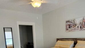 Une chambre à coucher avec un lit, une tête de lit en bois, un ventilateur de plafond et un tableau accroché au mur.