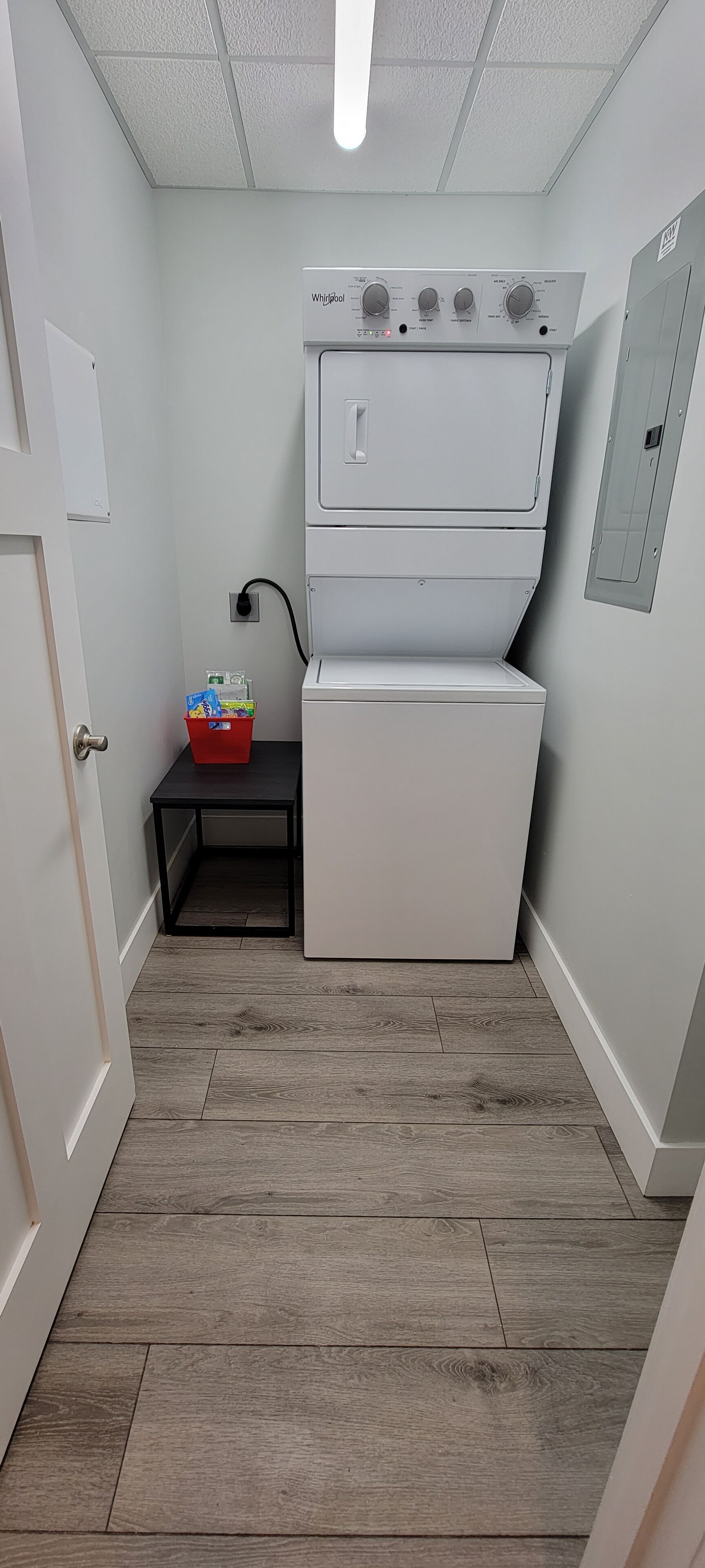 Una sala de lavandería con lavadora y secadora Whirlpool, una mesita con un cesto, y una puerta.