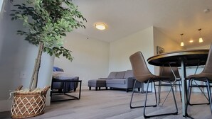 Un salon moderne avec une table de salle à manger ronde, deux chaises marron, un canapé gris et une plante en pot.