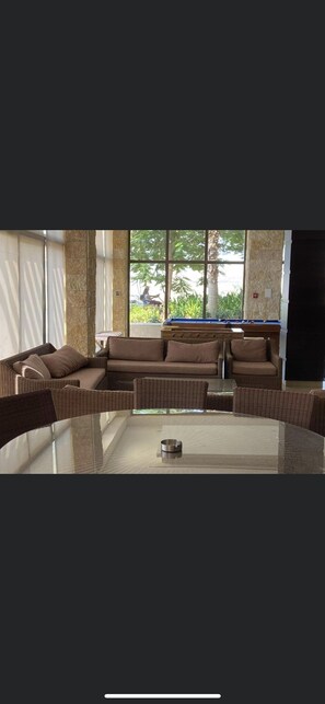 A modern living room with a glass coffee table, brown sofas, and a large window with a view of greenery. - Lovely 2 bedrooms serviced apartment with apool (Dead sea swemeh)