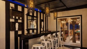 Una zona de bar con mostrador negro, taburetes blancos y lámparas de mimbre colgantes.