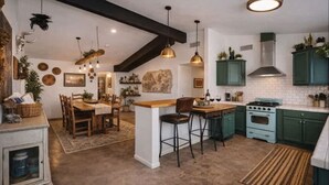 Una cocina con una isla central, sillas de madera, lámparas colgantes y armarios verdes.