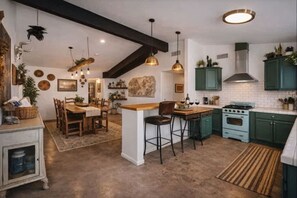 A kitchen with a central island, wooden chairs, pendant lights, and green cabinets.