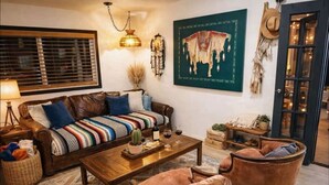 Una sala de estar acogedora con sofá, mesa de centro y sillones, una lámpara, un cactus y un cuadro en la pared.