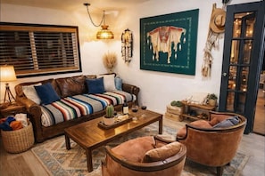 A cozy living room with a sofa, coffee table, and armchairs, a lamp, a cactus, and a painting on the wall.