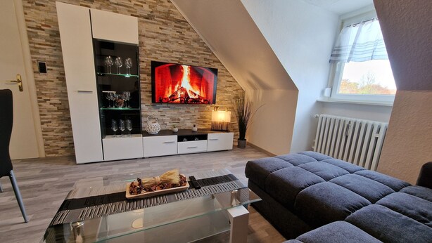 A modern living room with a fireplace, a sofa, and a TV mounted on a stone wall. - Exclusive and bright apartment in the centre (Kassel)