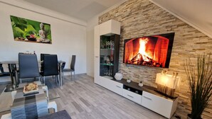 A modern living room with a stone wall, a flat-screen TV, a glass coffee table, and a dining area with chairs and a table. - Exclusive and bright apartment in the centre (Kassel)
