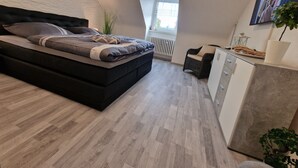 A modern bedroom with a large bed, a small desk, a radiator, and a window. - Exclusive and bright apartment in the centre (Kassel)