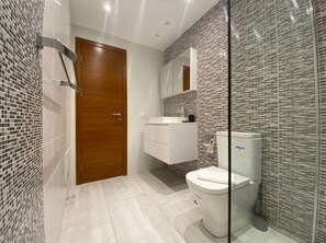 Un baño moderno con puerta de madera, tocador blanco y un inodoro con mampara de vidrio.