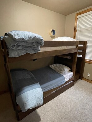 A bunk bed with a blue blanket and pillow, a wooden headboard, and a small mirror on the wall.