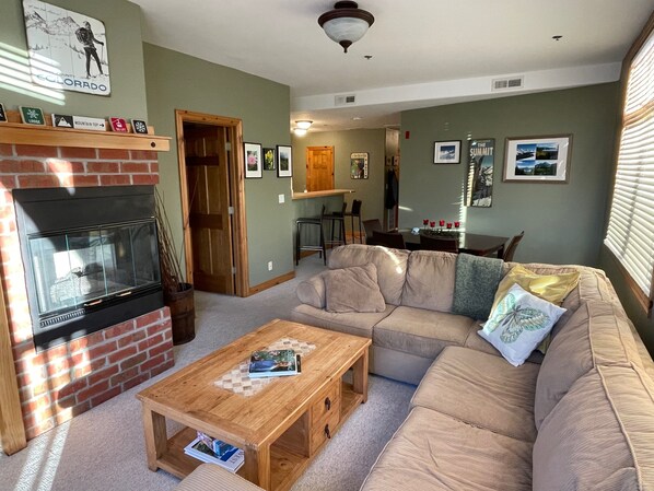 A living room with a fireplace, a sofa, a coffee table, and a dining area in the background.