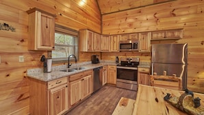 A wooden cabin kitchen with granite countertops, stainless steel appliances, and wooden cabinets.