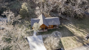 A log cabin with a steeply pitched roof, surrounded by a wooded area.
