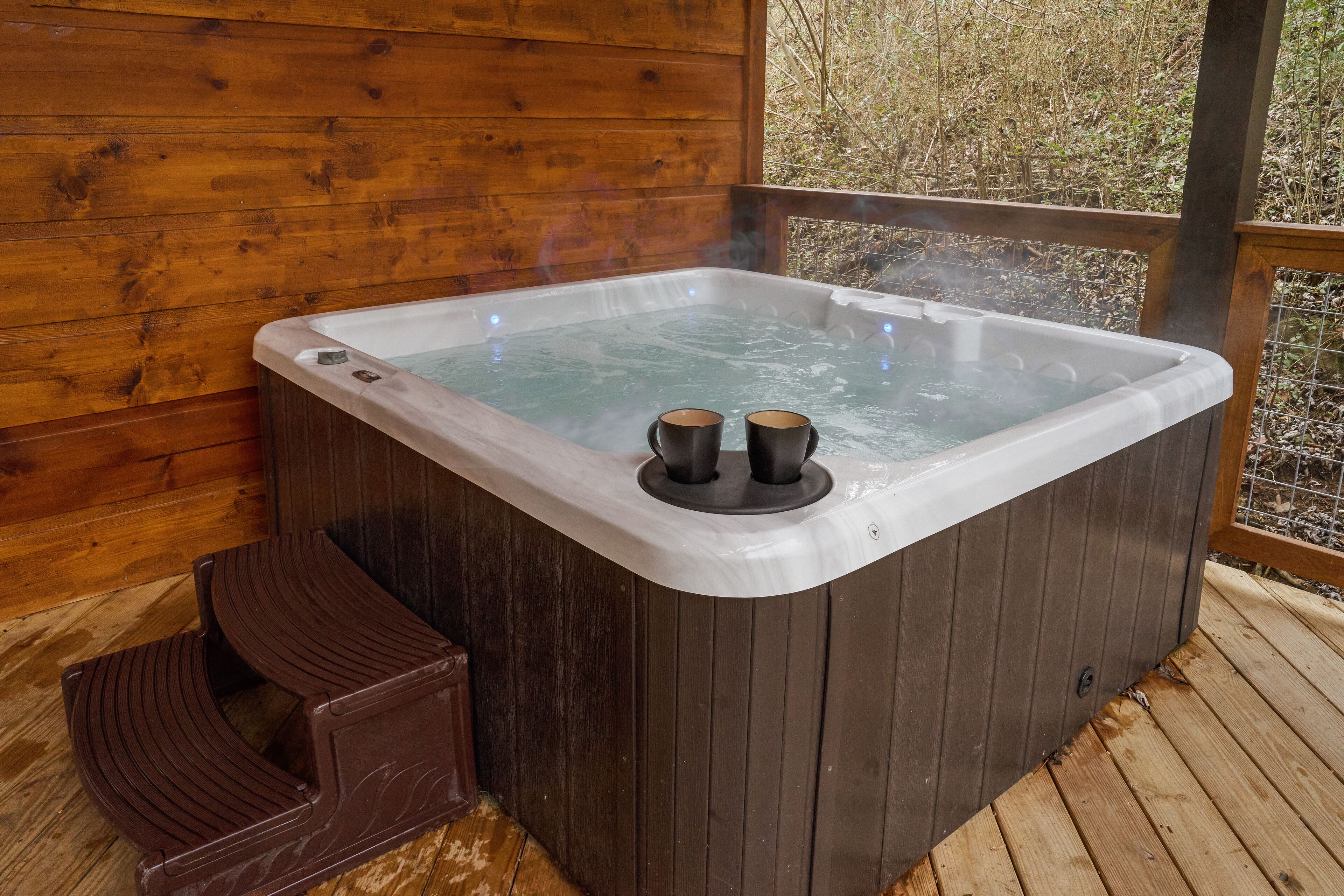 A wooden cabin with a hot tub, two cups on the tub, and a wooden deck.