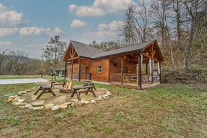 Eine rustikale Holzhütte mit verdeckter Veranda, Feuerstelle und Picknicktischen.
