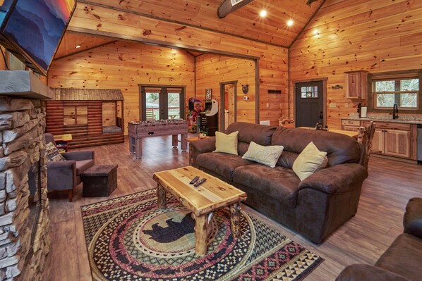 Ein gemütliches Blockhaus-Interieur mit Wohnbereich, Steinwand, Kamin und Küchenzeile.