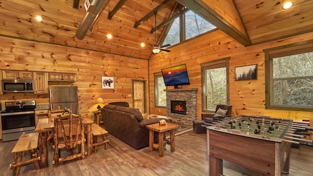 A cozy wooden cabin interior with a kitchen, living room, and a foosball table.
