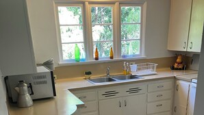 Een keuken met witte kastjes, een spoelbak, een raam met flessen en een koffiezetapparaat.