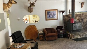 Een gezellige woonkamer met een open haard, een op de muur bevestigd hertenhuid, een ingelijst kunstwerk en een leren fauteuil.