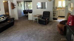 Een woonkamer met een open haard, een opgehangen hertenhoofd, een zwarte leren fauteuil en een keuken met een spoelbak en kastjes.