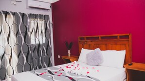 A hotel room with a bed, a nightstand, a wooden headboard, and a wall-mounted air conditioner.