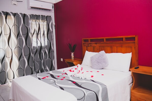 Une chambre d’hôtel comprenant un lit, une table de chevet, une tête de lit en bois et un climatiseur fixé au mur.