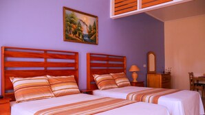 A room with two beds, wooden headboards, striped bedding, a painting on the wall, a mirror, and a wooden dresser.