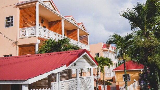 A multi-story building with balconies, a red roof, and a white fence.
