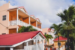 Un immeuble à plusieurs étages, doté de balcons, d’un toit rouge et d’une clôture blanche.